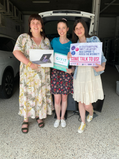A female staff member from GIVIT, along with two female staff members from Queenslanders with Disability Network holding a donated tablet and GIVIT sign