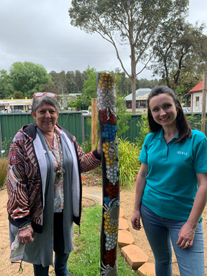 GIVIT Corporate Manager Caroline Odgers, smiling for a photo with Julie Nichols from Mogo Aboriginal Preschool, with a First Nations totem pole between them